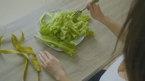 Woman sits at a table and eats cabbage leaves adheres to a diet Stock Footage 128645464