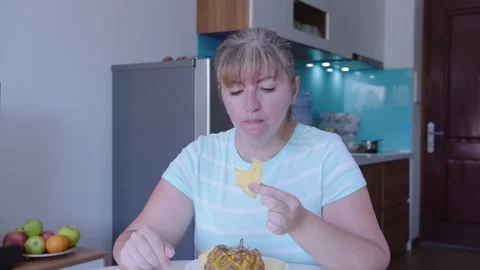 Woman sits at a table in front of a kitchen and eats a pineapple Stock Footage 319338558
