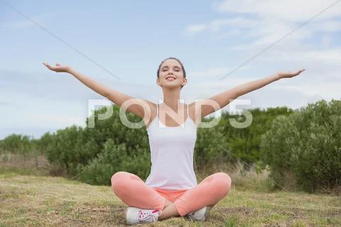 Woman sitting with arms raised on countryside landscape Stock Photos
