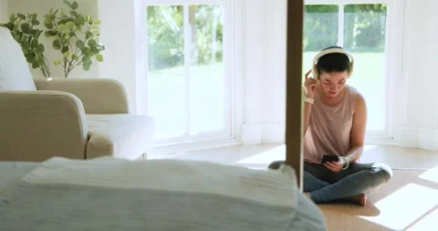 Woman sitting by bay window, tapping phone to start meditation, putting on Stock Footage 341938233