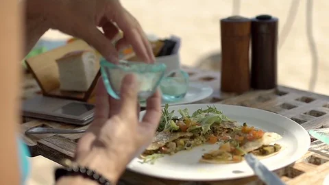 Woman sitting on the beach and adding spices to her food, steadycam shot Stock-Footage 80939619