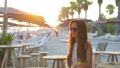 Woman Sitting at a Beach Table, Basking in Sunset Rays Stock Footage 314699211