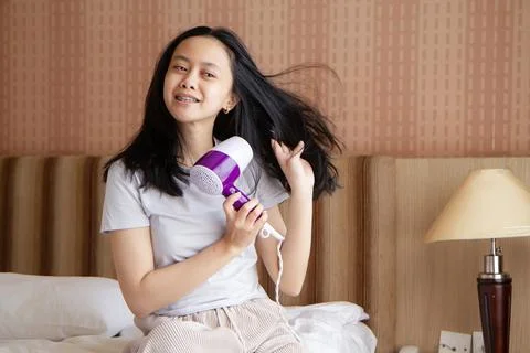 Woman sitting on bed blow drying hair Stock Photos