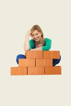 Woman sitting behind stack of bricks, smiling, portrait 写真素材