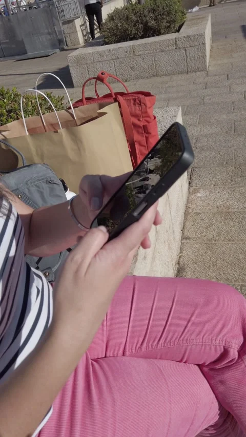 A woman is sitting on a bench and using her cell phone, writes a text messa.. Stock Footage 324923101