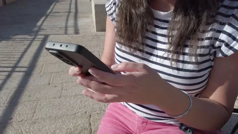 A woman is sitting on a bench and using her cell phone outdoors. Stock Footage 324923123