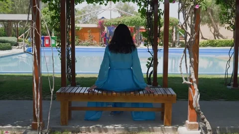 Woman sitting on bench overlooking pool in garden pergola Stock Footage 345700637