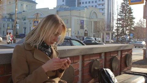 Woman sitting on bench using smart mobile phone reading at sunny city street 스톡 동영상 75365765