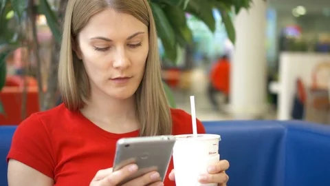 Woman sitting in cafe using her smartphone, chatting with friends drinking cola Video stock 76848048