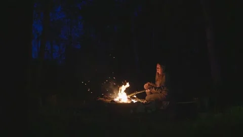 The woman sitting by the campfire in the forest and moving burning logs. Stock Footage 277708946