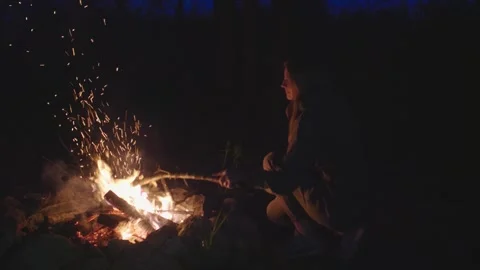 The woman sitting by the campfire in the forest and moving burning logs. Stock Footage 277709468