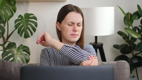 Woman sitting at computer and experiencing pain and discomfort in elbow joint Stock Footage 252071413