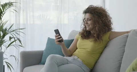Woman sitting on the couch and using her smartphone Stock Footage 162377286