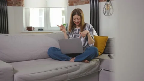 Woman sitting on couch dancing using laptop looking at screen smiling chatting Stock Footage 133744519