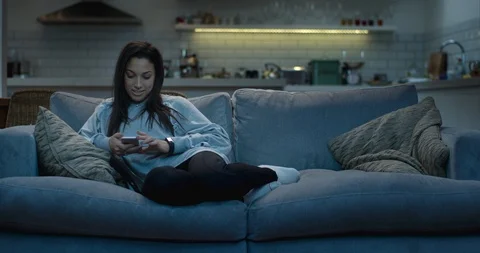 Woman sitting on a couch using her mobile phone to text a friend. 스톡 동영상 87604635