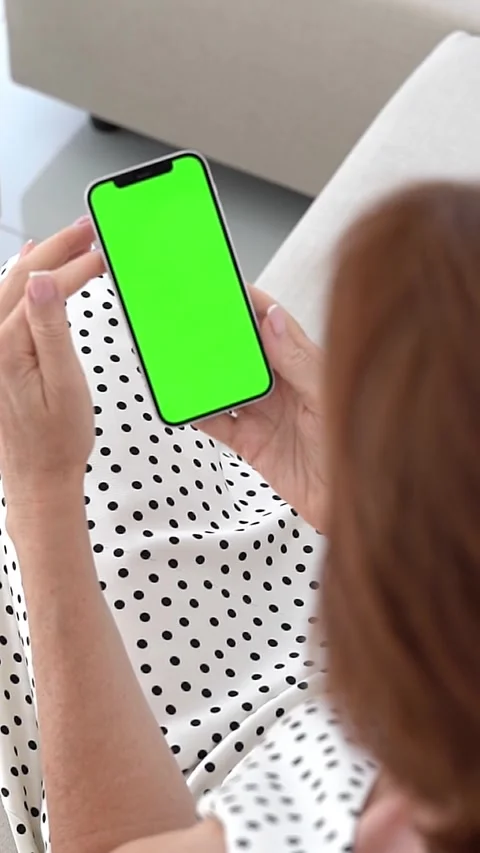 Woman Sitting on Couch Using Smartphone, With Vertical Green Chroma Key Screen Stock Footage 300678067