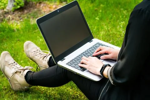 A woman is sitting on the grass while using laptop computer Stock Photos