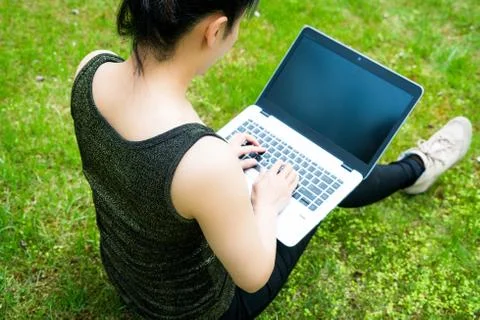 A woman is sitting on the grass while using laptop computer Stock Photos