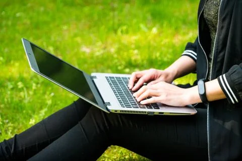A woman is sitting on the grass while using laptop computer Stock Photos
