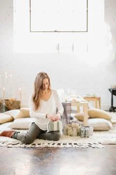 A woman sitting on the ground by a stack of parcels, opening presents. 스톡 사진