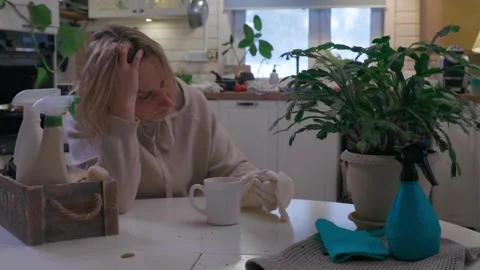 Woman sitting at kitchen table taking a break during house cleaning, drinking co Stock Footage 329579202