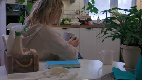 Woman sitting at kitchen table taking a break during house cleaning, drinking co Video stock 329579322