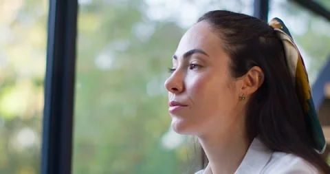 Woman sitting by large window, pausing then opening eyes, turning to camera Stock Footage 340614065