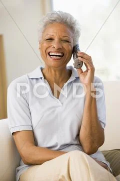 Woman sitting in living room using telephone and smiling Stock-Fotos