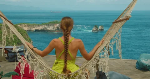 Woman Sitting In Macrame Hammock Facing Deep Blue Ocean At Nusa Penida Cliff In Stock Footage 327498252