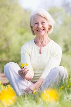 Woman sitting outdoors smiling and holding a Buttercup flower Stock Photos