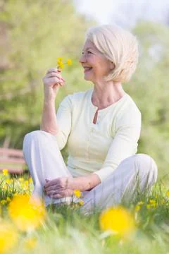 Woman sitting outdoors smiling and holding a Buttercup flower Stock Photos
