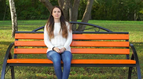 Woman sitting on a park bench and looking at the camera. 4K Stock Footage