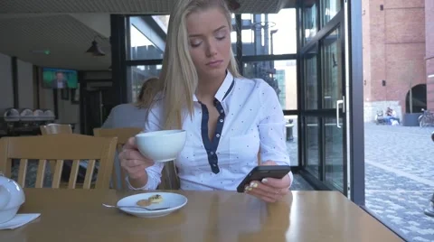 Woman sitting in the restaurant. She is using mobile phone and drinking coffee. Stock Footage 62128570