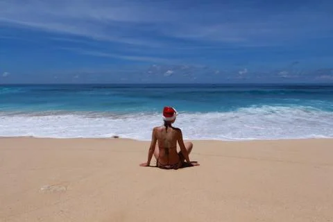 Woman is sitting with Santa's red hat on a tropical beach. Foto stock