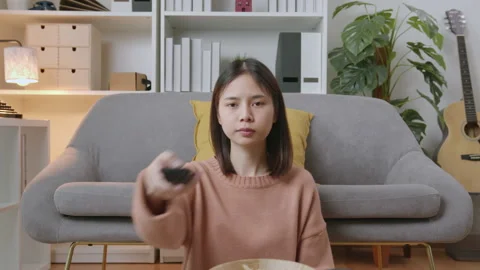 Woman sitting at the sofa and holding the TV remote to watch movies. 스톡 동영상 135293553