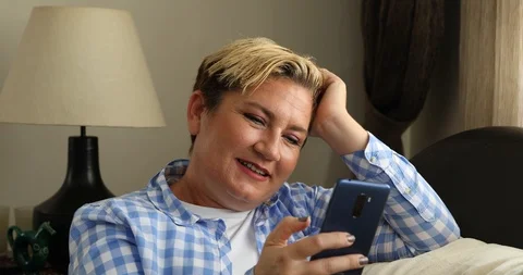 Woman sitting on sofa and using smart phone at home 4 Stock Footage 117739251