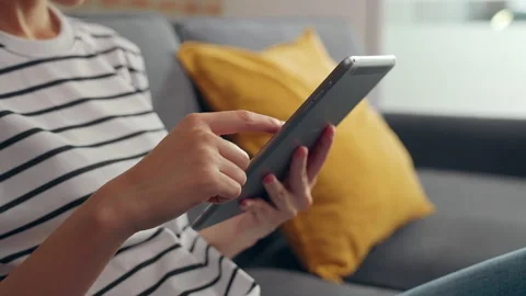 Woman sitting on the sofa and using digital tablet online social. 스톡 동영상 153972492