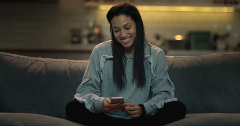 Woman sitting on a sofa in a cozy living room texting her friends Stock Footage