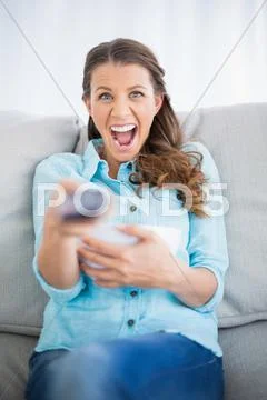 Woman sitting on sofa screaming while watching tv Stock Photos