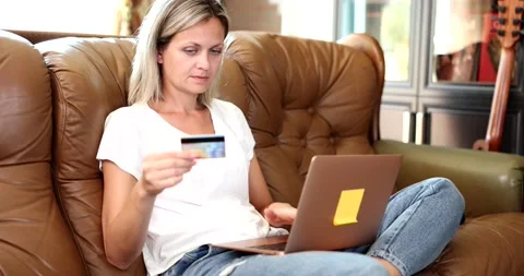 Woman is sitting on sofa using laptop computer and shopping online with credit Vídeo Stock 217806736