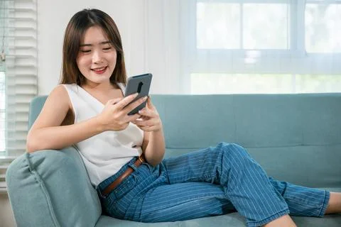 Woman sitting on sofa using mobile smart phone at living room Stock Photos