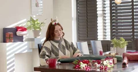 Woman sitting at table in argyle sweater, holiday spirit driving wrapping with Stock Footage 343889400