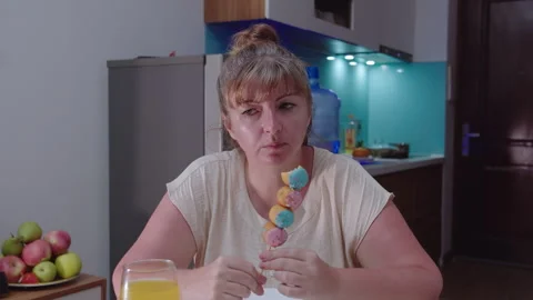 A woman sitting at a table eats curd balls covered with pink and blue glaze Stock Footage 329940041