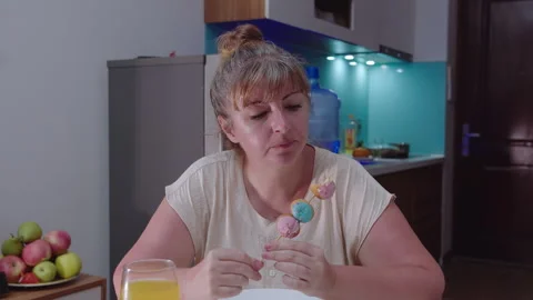 Woman sitting at a table eats curd balls covered with pink and blue glaze Stock Footage 329940363