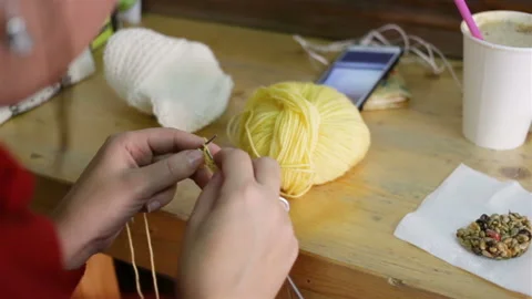 A woman is sitting at a table knitting, on the table: a Cup of coffee, a smartph Video stock 144109700