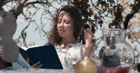 A woman is sitting at a table reading a book Stock Footage 284344000