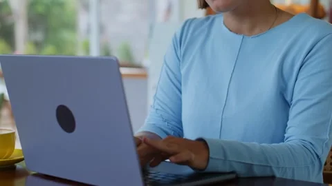 A woman is sitting at a table using a laptop computer for leisure and fun Stockbeeldmateriaal 268807900