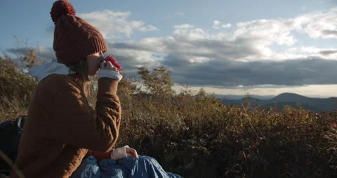 Woman sitting on top of mountain drinking from a mug and watching the sunset Stock Footage 141015965