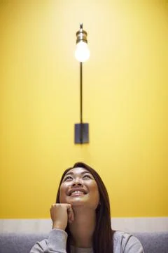 Woman Sitting Under Light Bulb In Office Suggesting Inspiration Or Idea Stock Photos