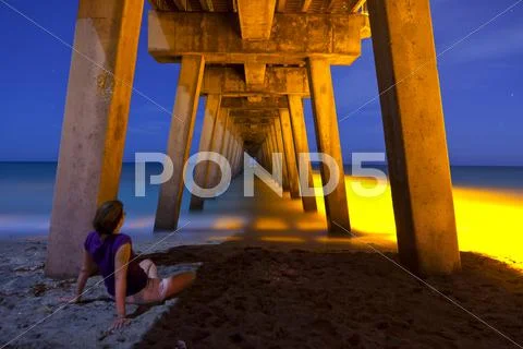Woman sitting under pier at night Stock Photos